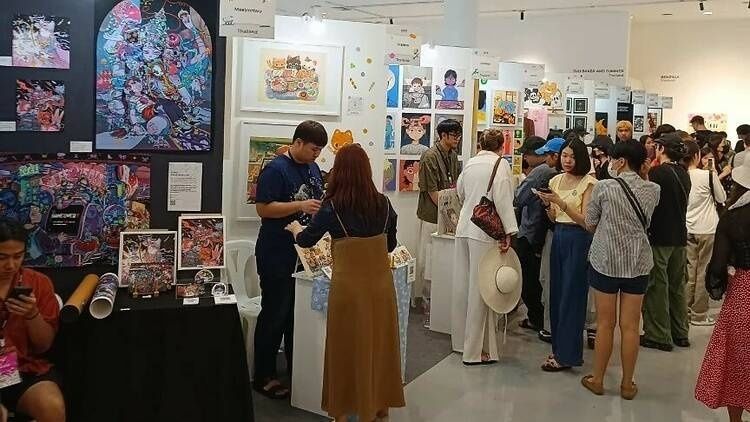 Crowded comic art festival hall with illustrated prints and artist booths